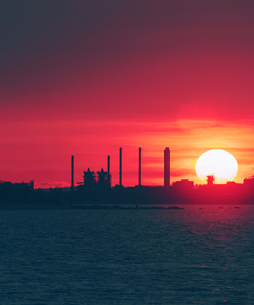Oil refinery next to the water with bright setting sun.