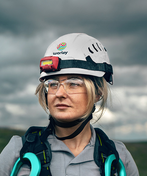 Woman wearing a Worley safety helmet with wind turbines in background.
