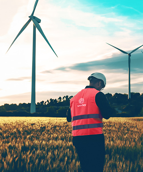 Person wearing Worley PPE next to a wind farm.