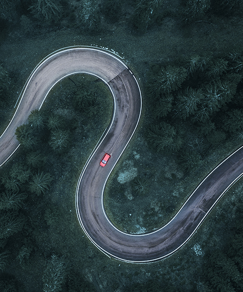 Aerial view of a bright car on a winding road through the forest.