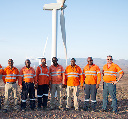 8 people of Worley standing in front of wind turbines at the Lake Turkana Wind Farm.