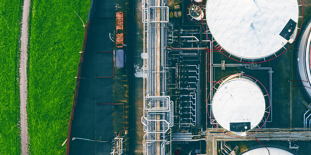 Aerial view of a refinery wth white tanks and green grass.