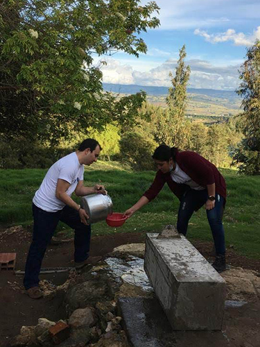 Two volunteer workers pouring water into a bowl.